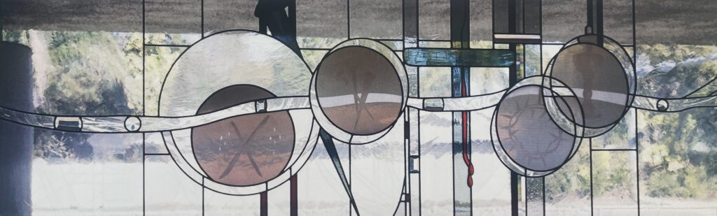 stained glass window of cross with blood dripping from it and gray circles etched with a crown of thorns, nails, and whips. 