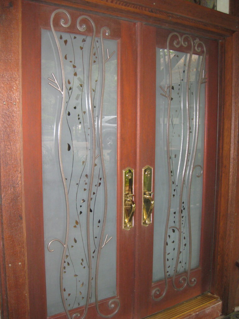 wood doors with glass panels that have etched leaves going up them with a metal detail.