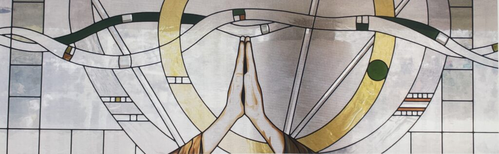 stained glass window of two hands folded in prayer. 