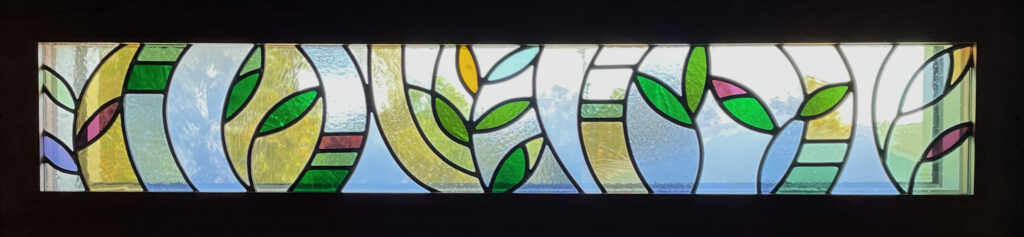 stained glass window of abstract leaves with a green, gold, blue, and purple color palette.