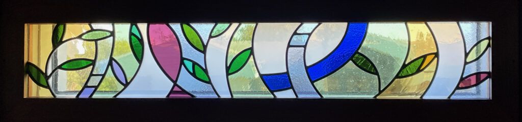 stained glass window of abstract leaves with a green, gold, blue, and purple color palette.