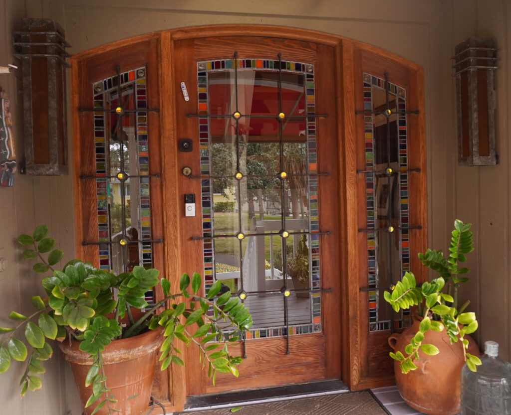 outside view of front door, metal grid over top of the glass has circular dichroic glass pieces in it, appearing yellow from the outside. 