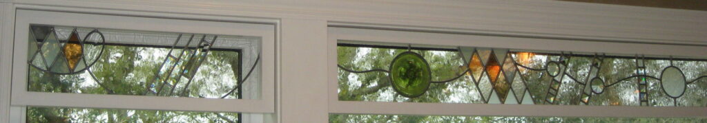 transom stained glass window that abstractly depicts a journey with triangles for mountains, wavy  lead lines for water, green circle for earth.